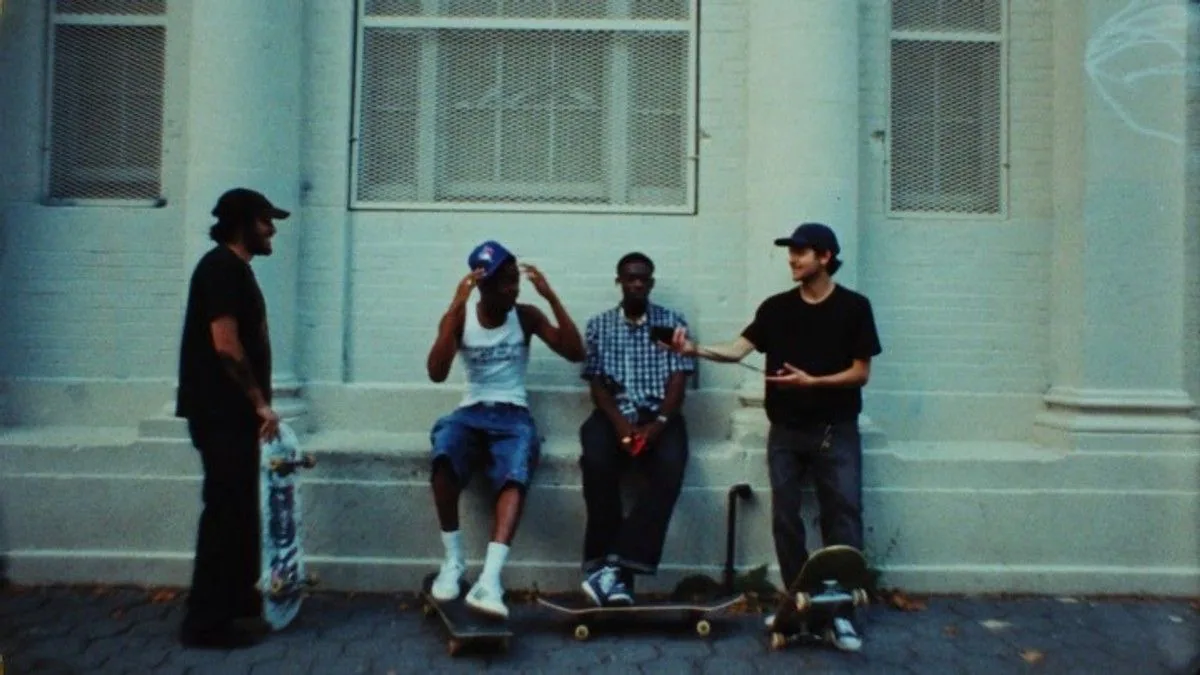 Four skaters with their boards, against a pale brick wall